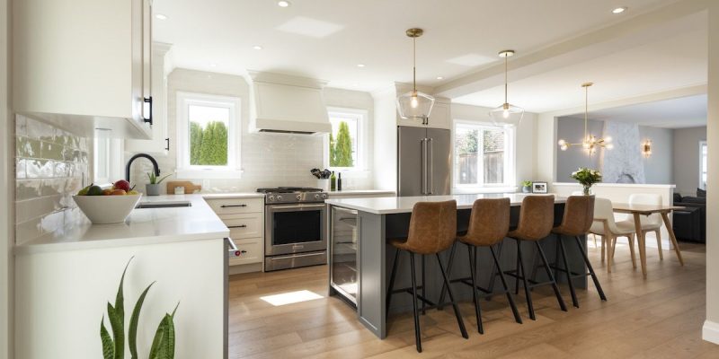 Open kitchen with stainless appliances, light cabinets, and a grounding stone grey kitchen island with bar stools.